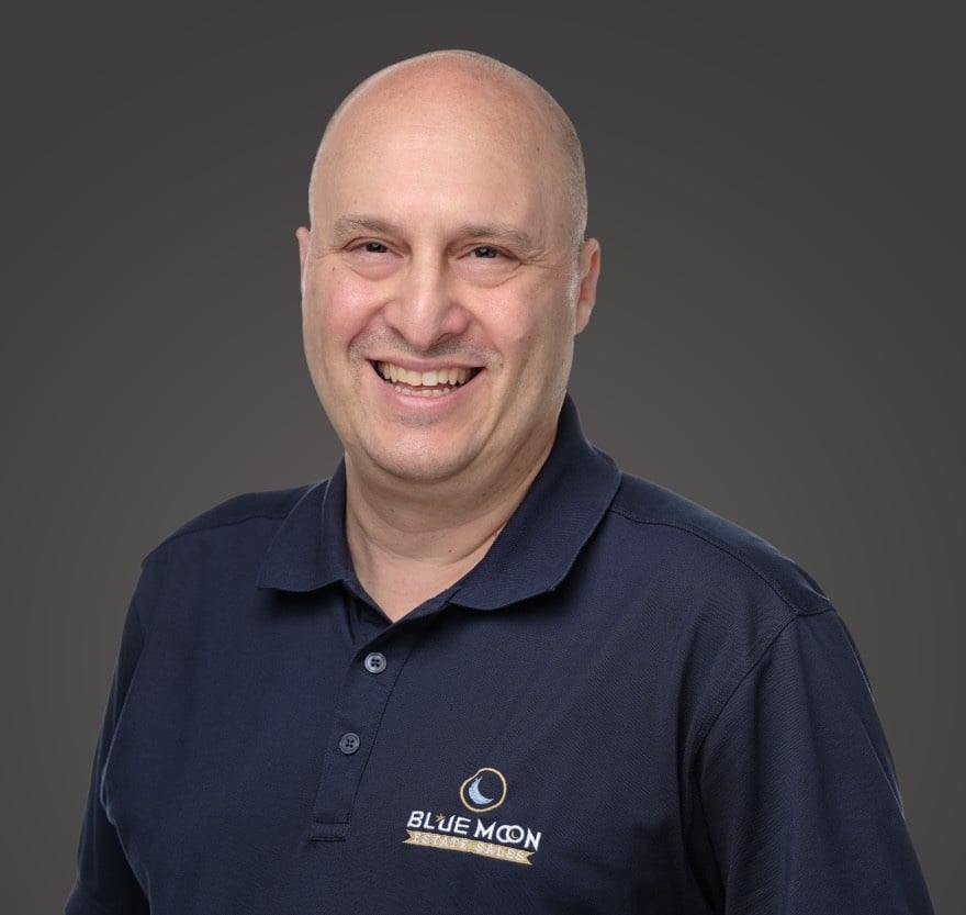 A smiling person wearing a dark blue polo shirt with the "Blue Moon" logo on it, against a gray background.