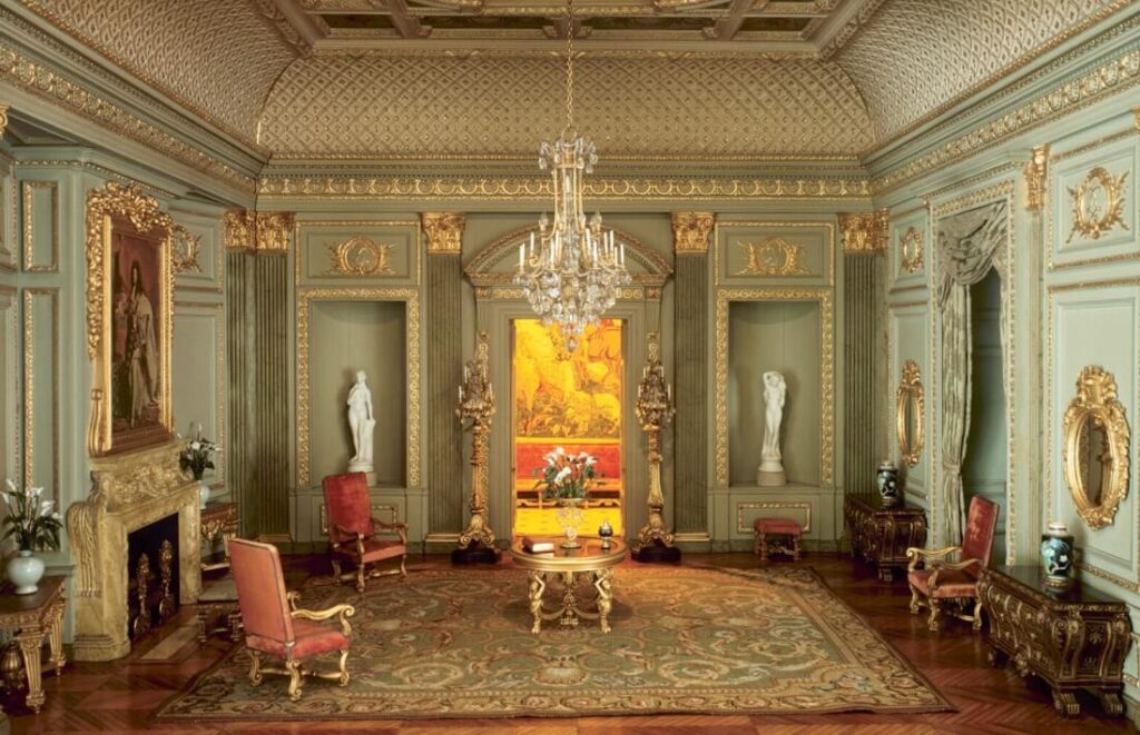 A vintage living room with furniture, a fireplace, glass chandelier and other decorations.
